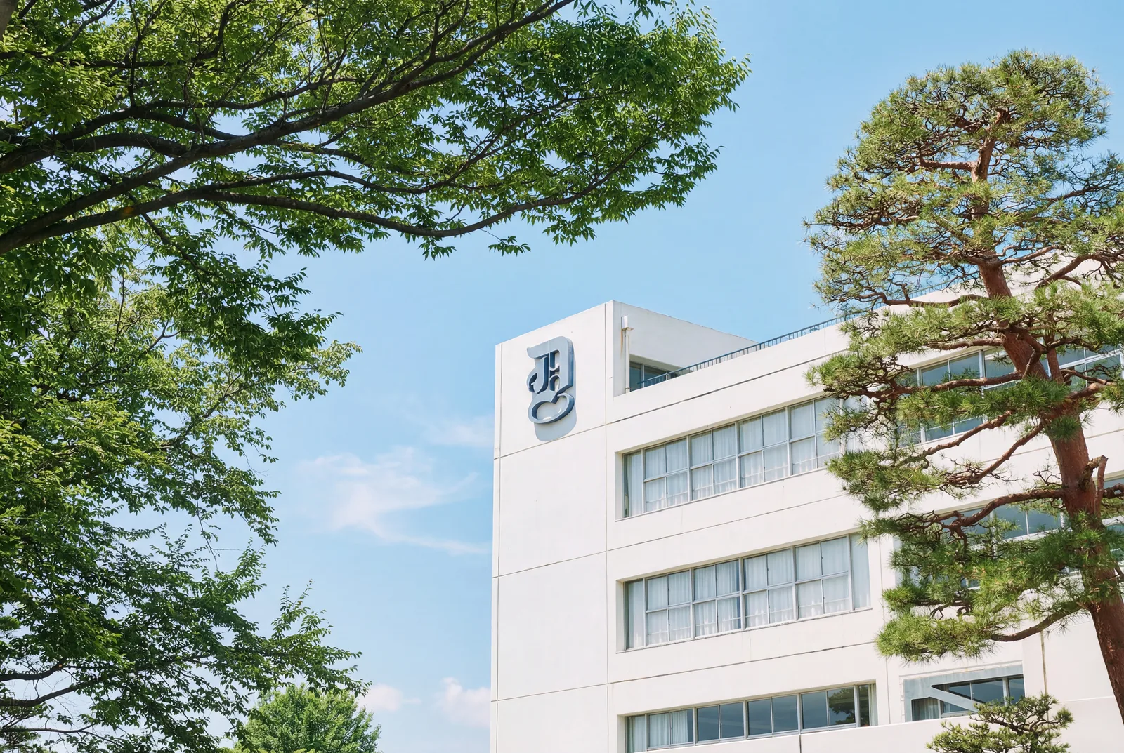 獨協埼玉中学高等学校の校舎。青空の下、木々の間から校章を掲げた白い校舎が見えている