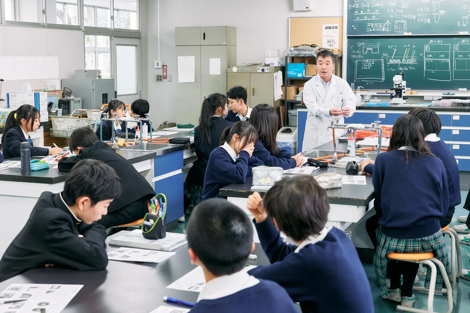 獨協埼玉中学高等学校の理科の授業。実験室で白衣の教員が説明し、生徒が実験台に向かっている
