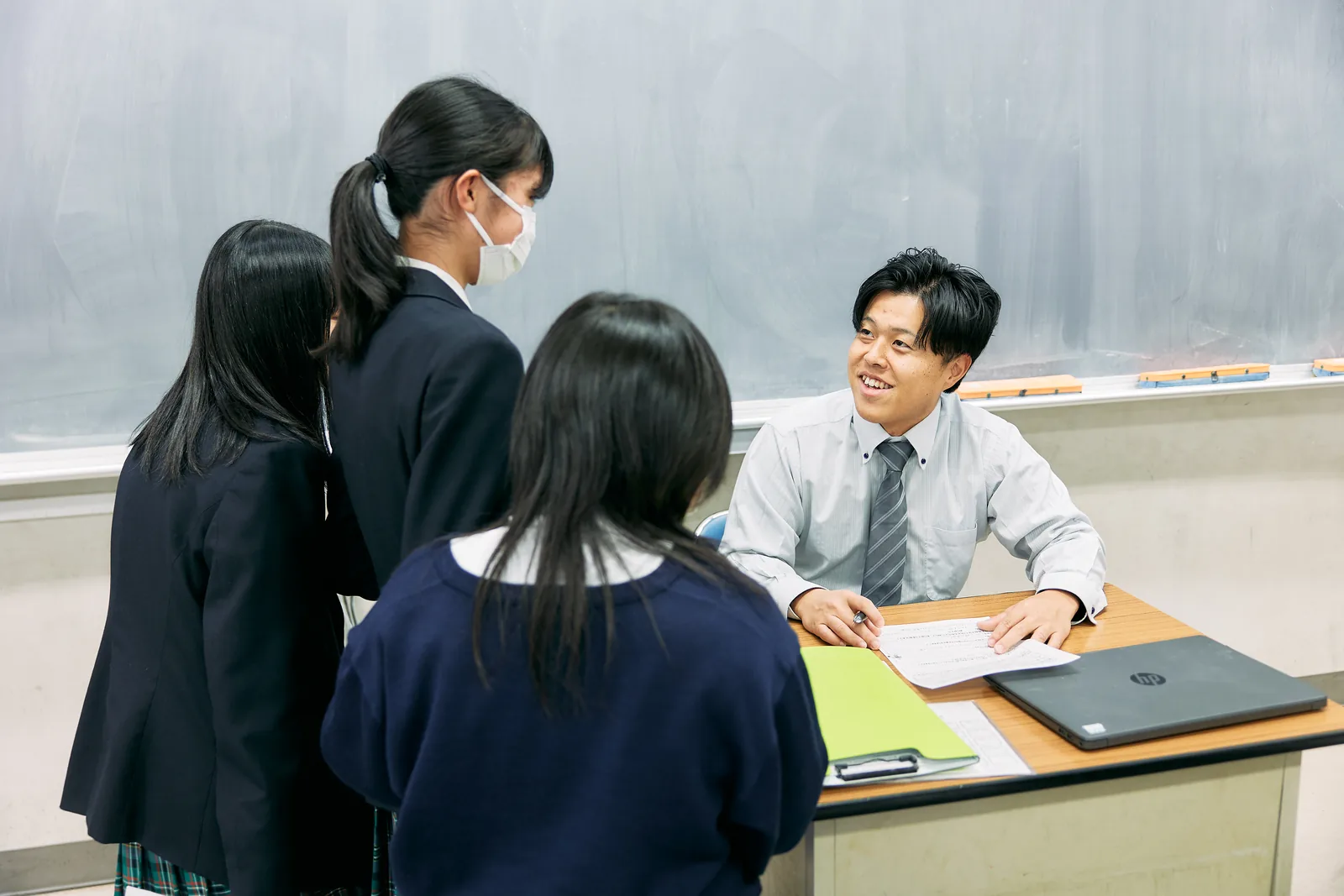獨協埼玉中学高等学校の教室で、机に向かう教員と3人の生徒が向かい合って話している