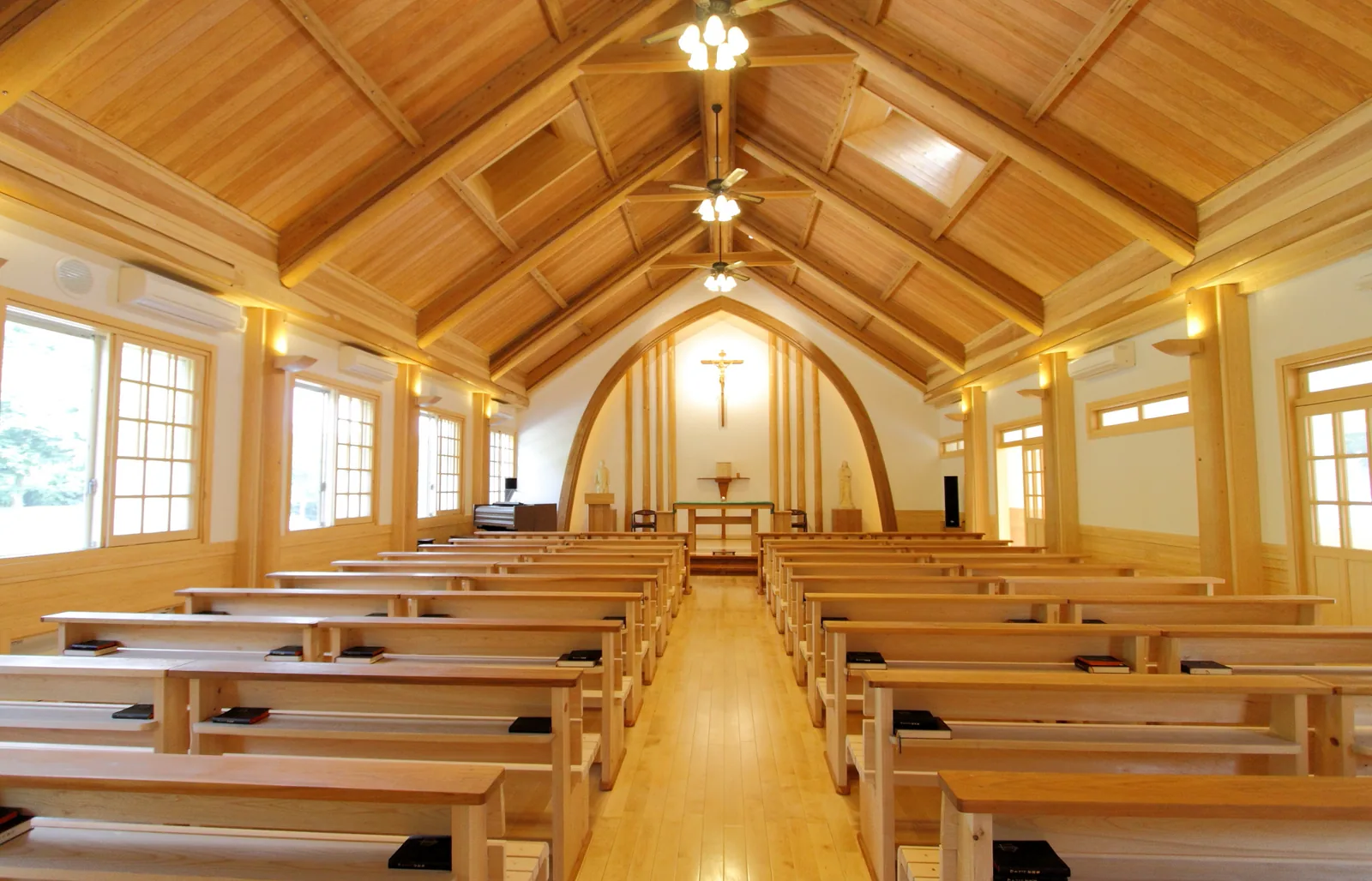 聖園女学院中学校・高等学校の聖堂の内部。木の梁が組まれた天井の下に木の長椅子が並び、正面に十字架が掲げられている