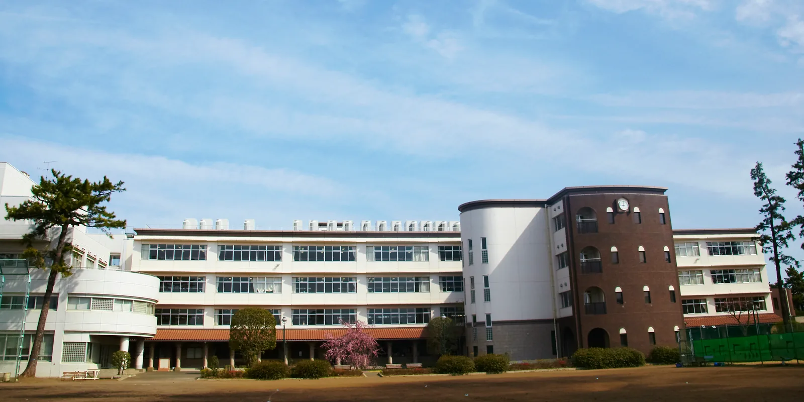 相模女子大学中学部・高等部の本校舎をグラウンドから見た様子。3階建ての校舎に大きな窓が並び、右手にれんが張りの時計塔が建つ