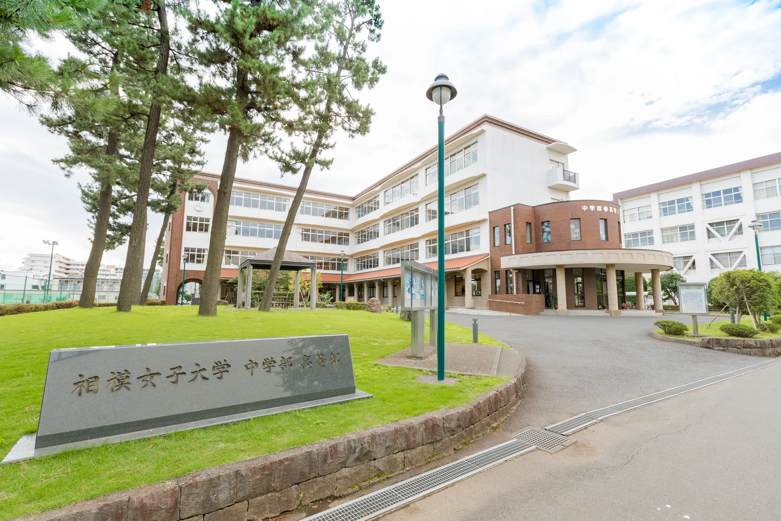 相模女子大学中学部・高等部の本校舎。手前の芝生広場に校名を刻んだ石碑とあずまやがあり、奥にれんが張りの円形の玄関と校舎が並ぶ