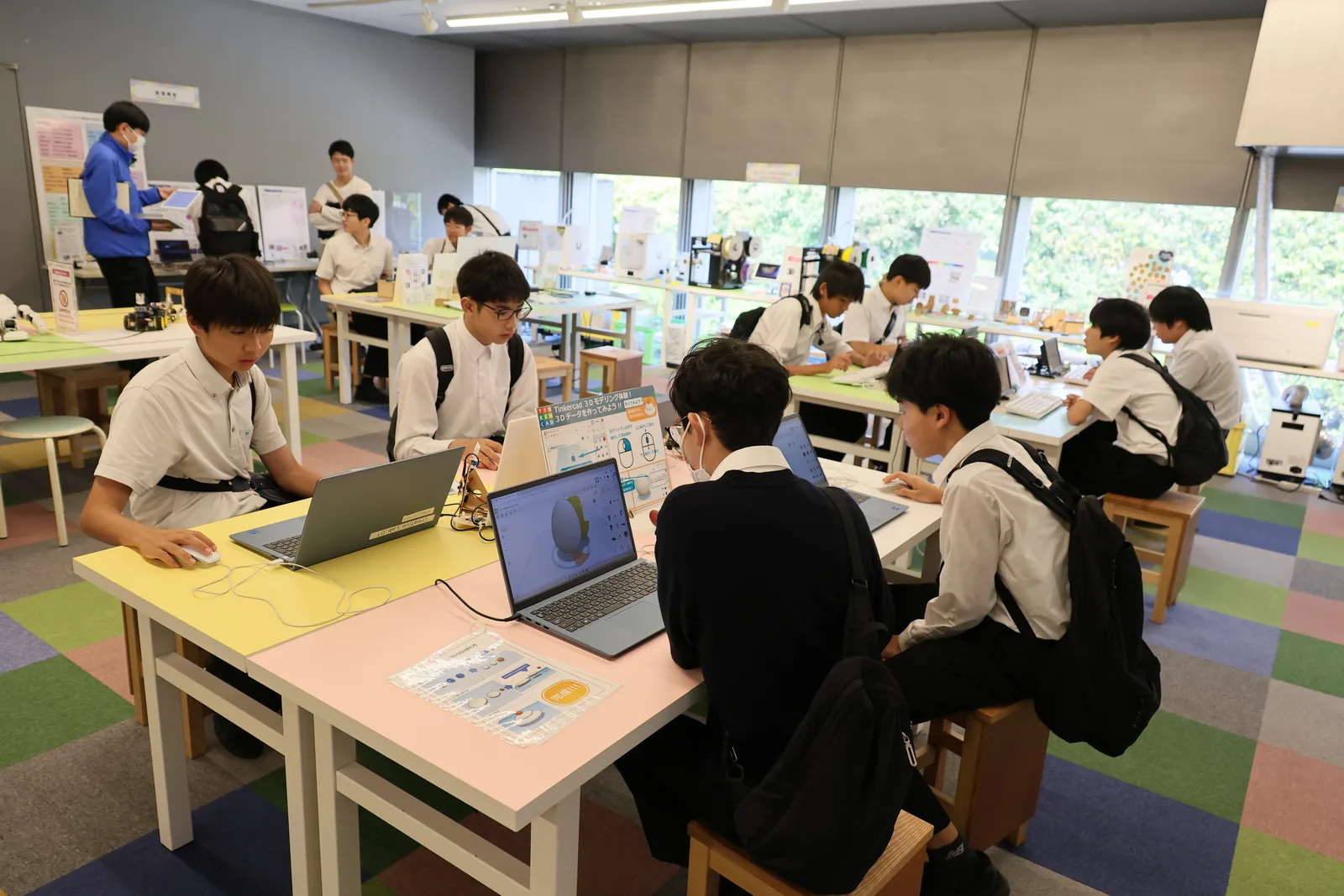 東京都市大学付属中学校・高等学校の教室での活動。生徒がノートパソコンを開いて作業し、机や棚に制作物が並んでいる